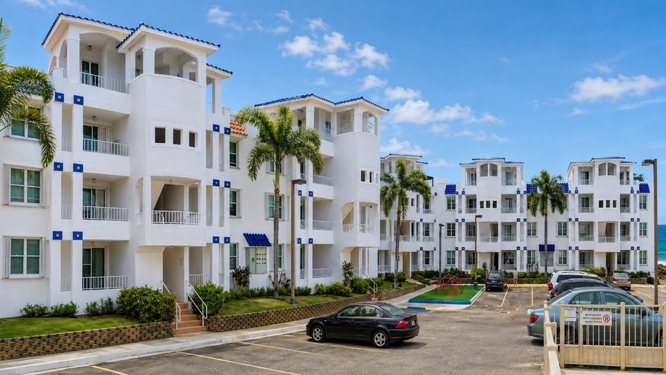 The white three-storey condominium buildings with blue trim, palms and parking
