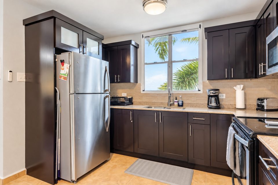 The stainless refrigerator beside the window, counters and sink along the wall