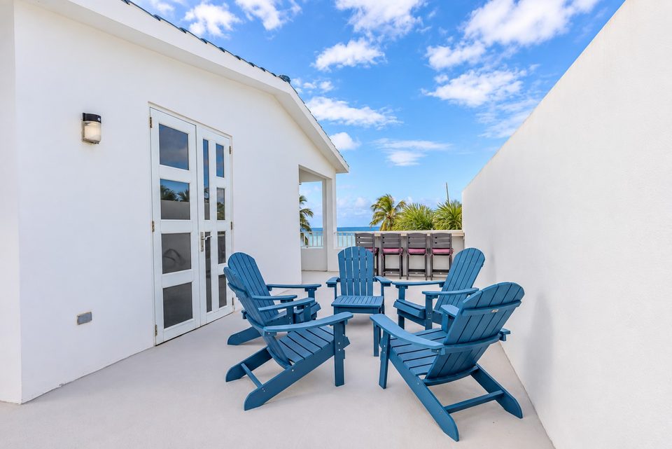 The rooftop terrace: blue Adirondack chairs around a low table, white French doors, the counter and stools at the far end and a glimpse of the ocean