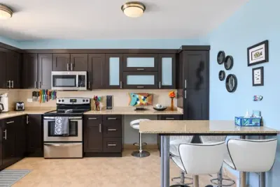 Cocina completa: estufa, microondas, gabinetes oscuros y barra con dos banquetas blancas