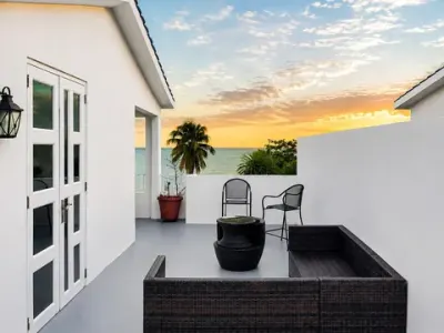Terraza privada en la azotea: puertas francesas blancas, muebles de mimbre, dos sillas junto a la pared, palmas y el Atlántico al fondo