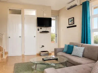 Entrada de la sala con televisor en la pared, mesa de cristal y cortinas turquesa